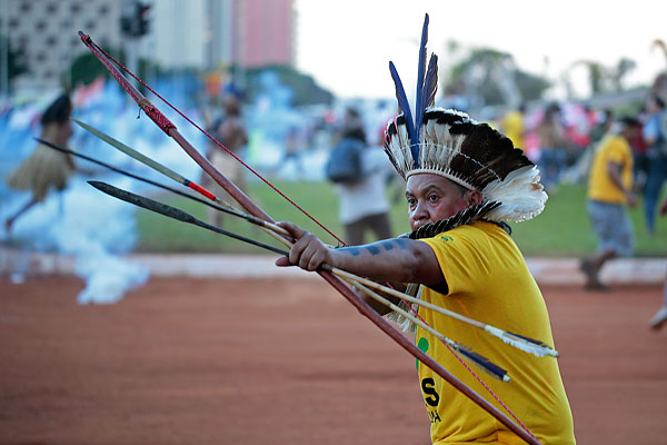 Бразильский индеец направляет свою стрелу в полицейских, которые пытаются помешать демонстрантам попасть на стадион Манэ Гарринчи.