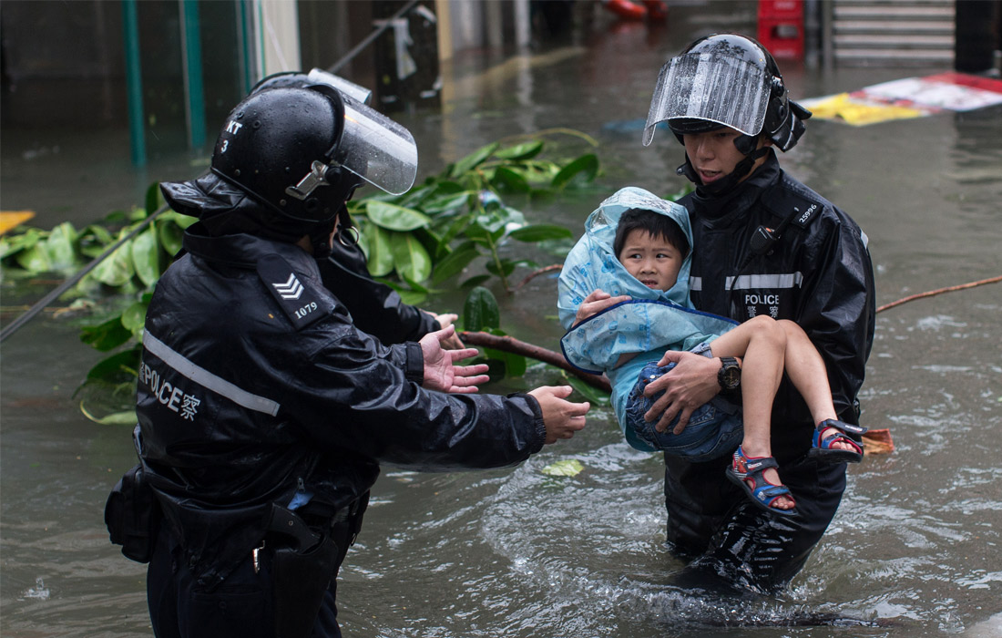Спасение людей при чрезвычайных ситуациях. Тайфун Мангхут. Полицейский спасает ребенка. Полицейский помогает ребенку.