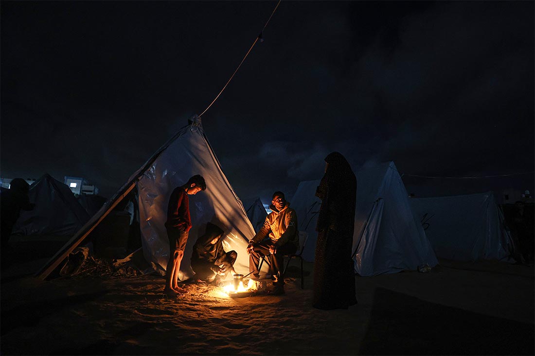 Лишенные домов палестинцы греются у палаток в лагере беженцев в Газе